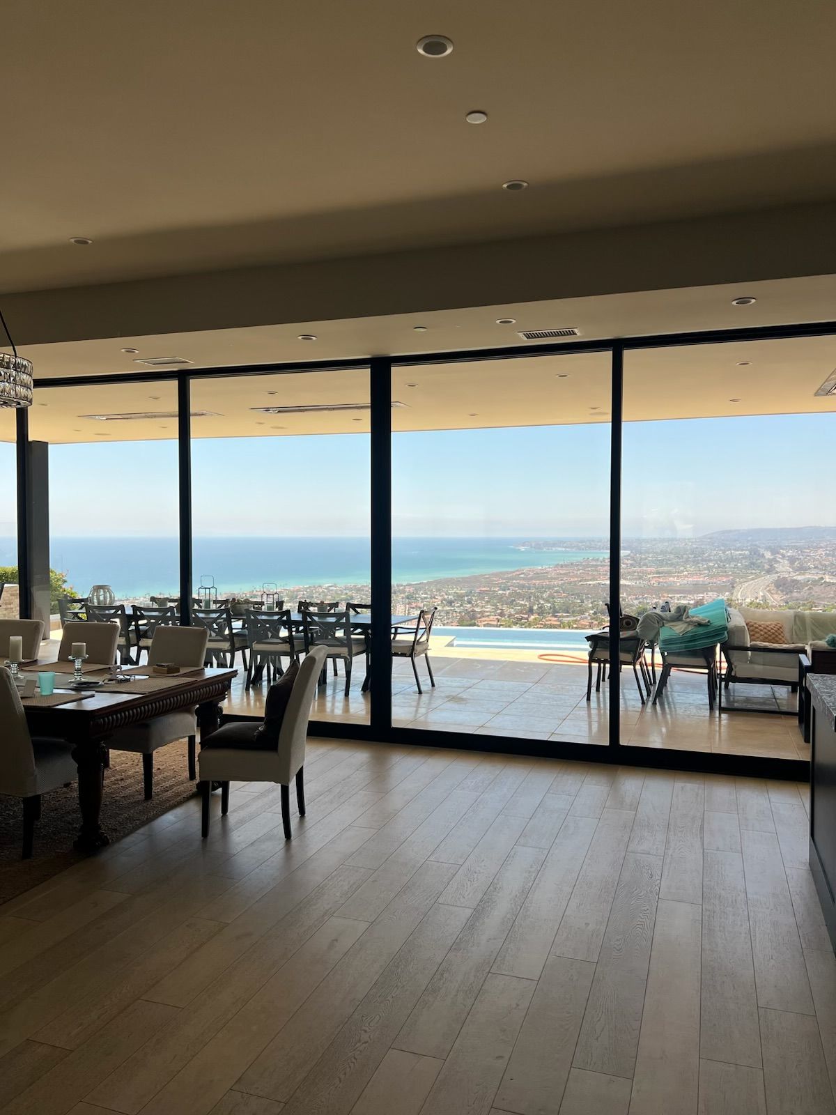 Spacious modern dining room with floor-to-ceiling windows overlooking a pool and coastal city view