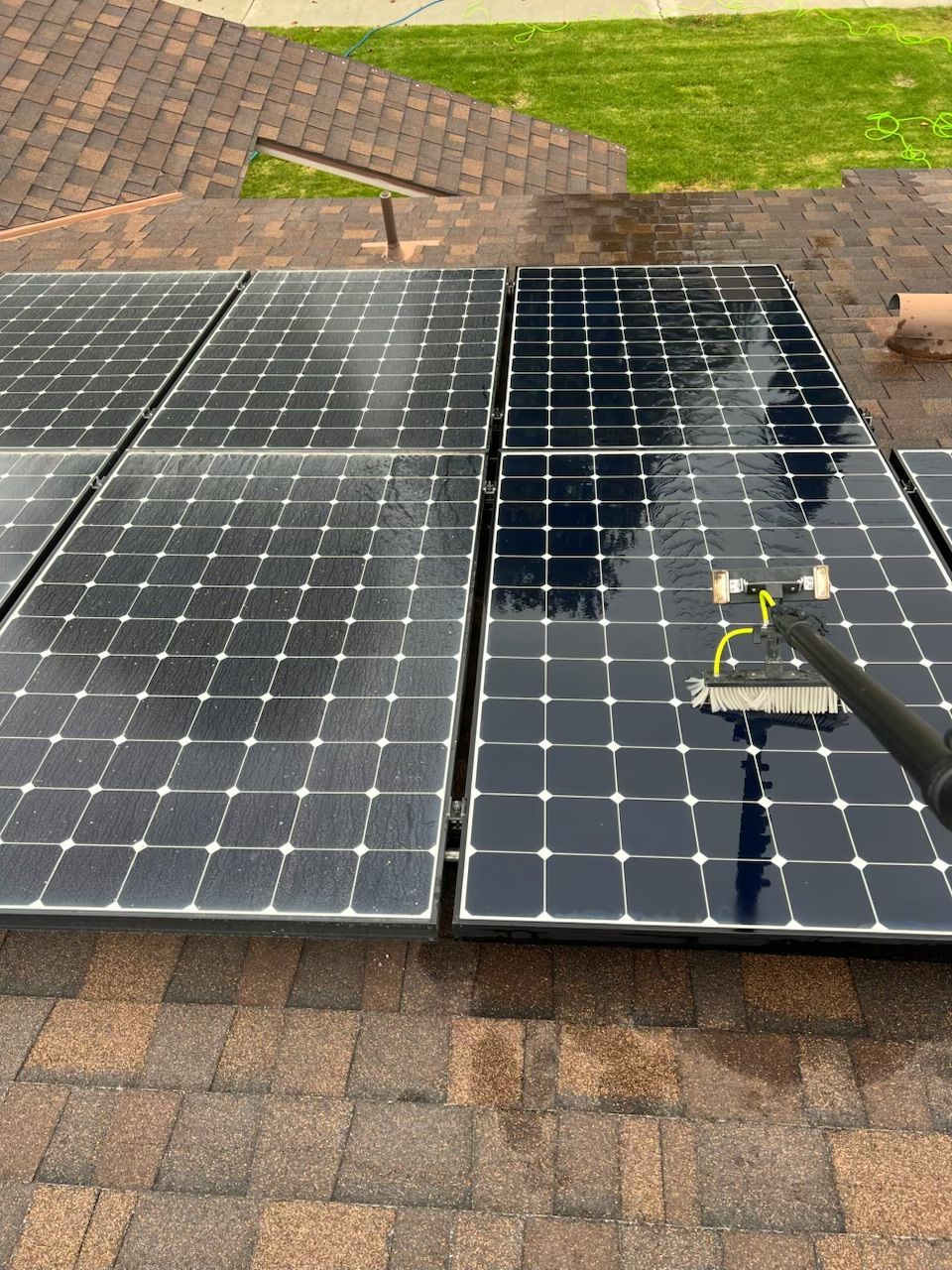 Solar panels on a shingled rooftop, with water streaks and a cleaning brush on the right panel.