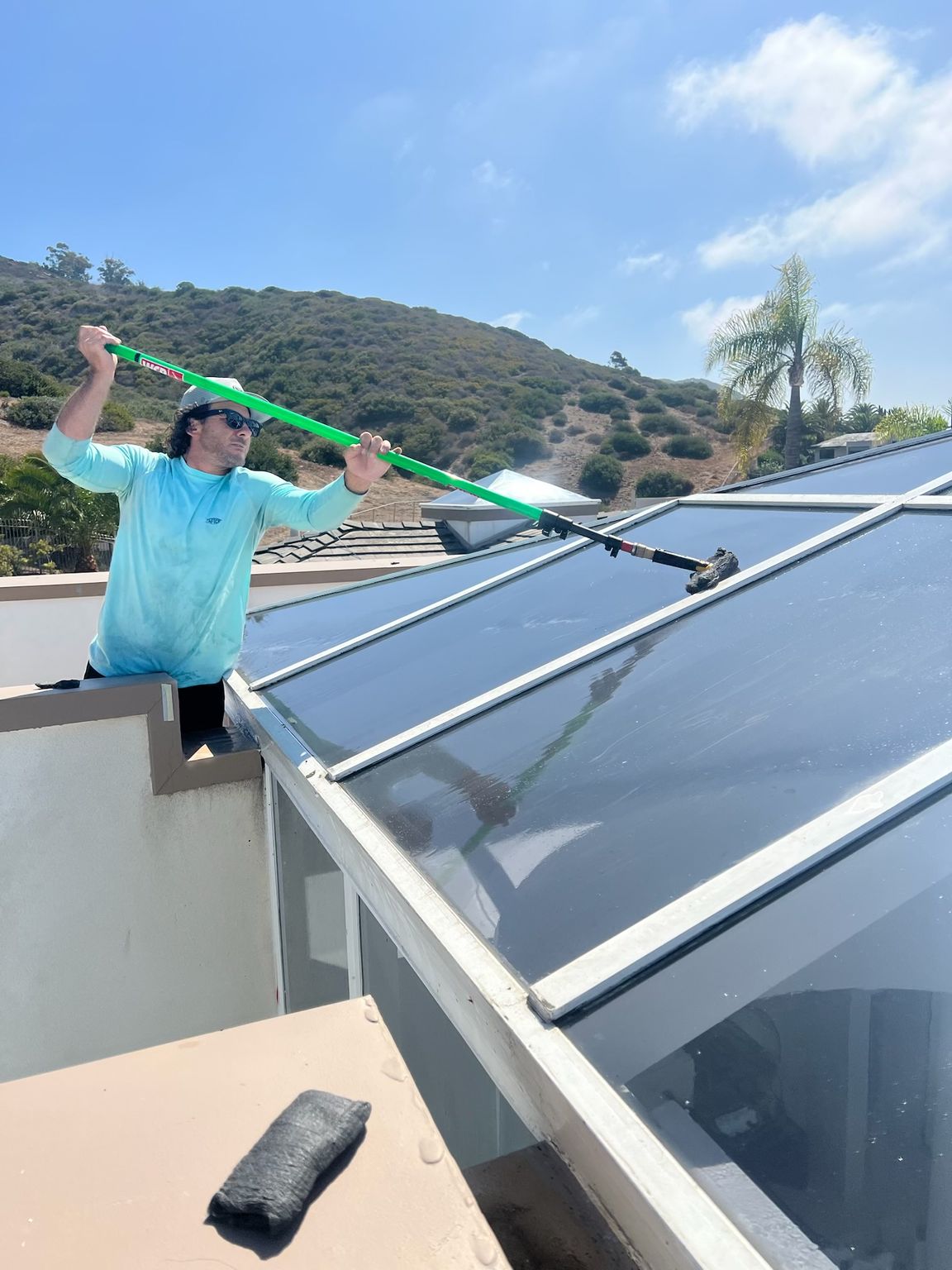 Person cleaning solar panels on a rooftop with a green pole under a sunny sky.
