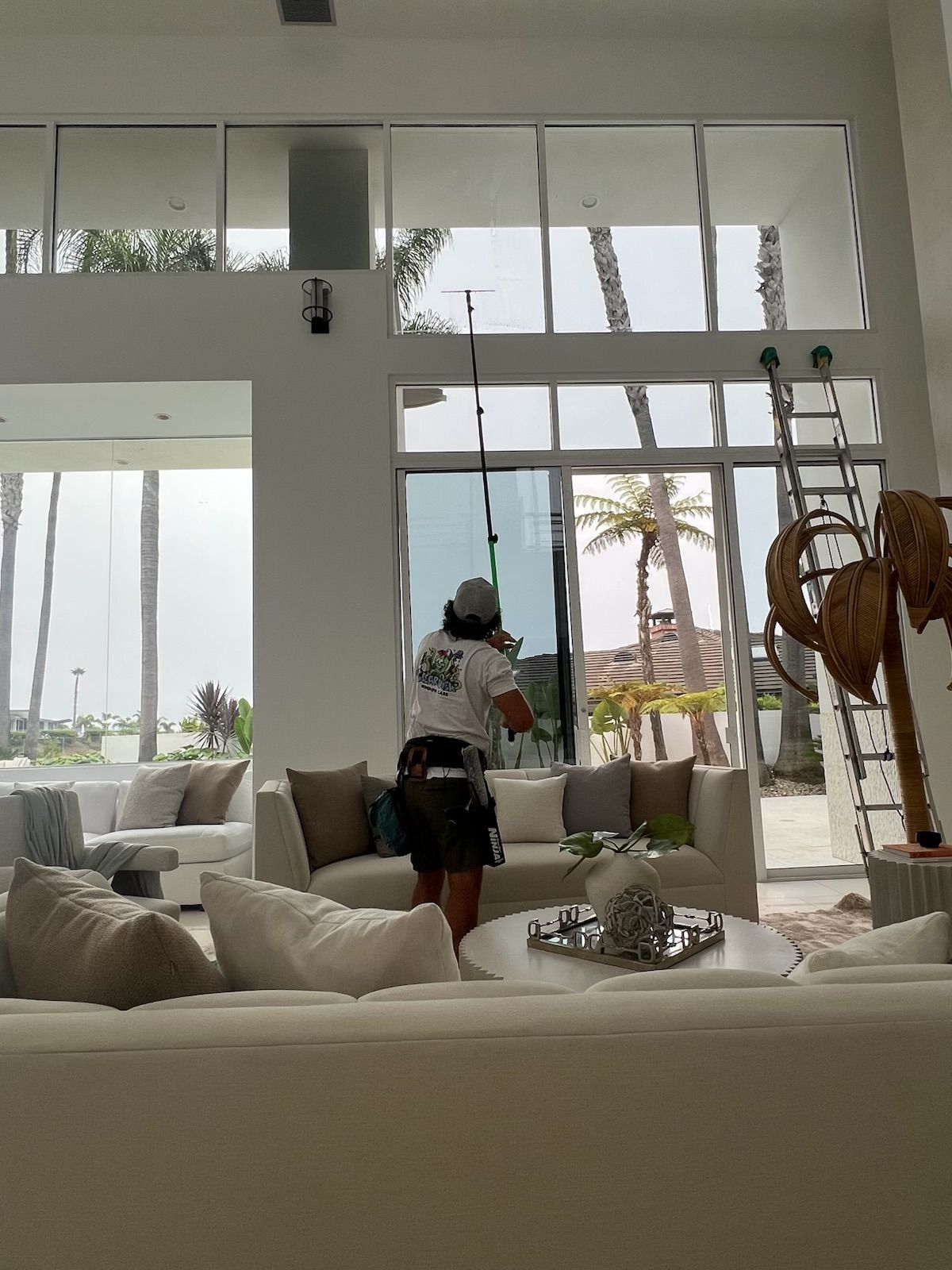 Bright living room with a person standing by large windows and a view of palm trees outside.
