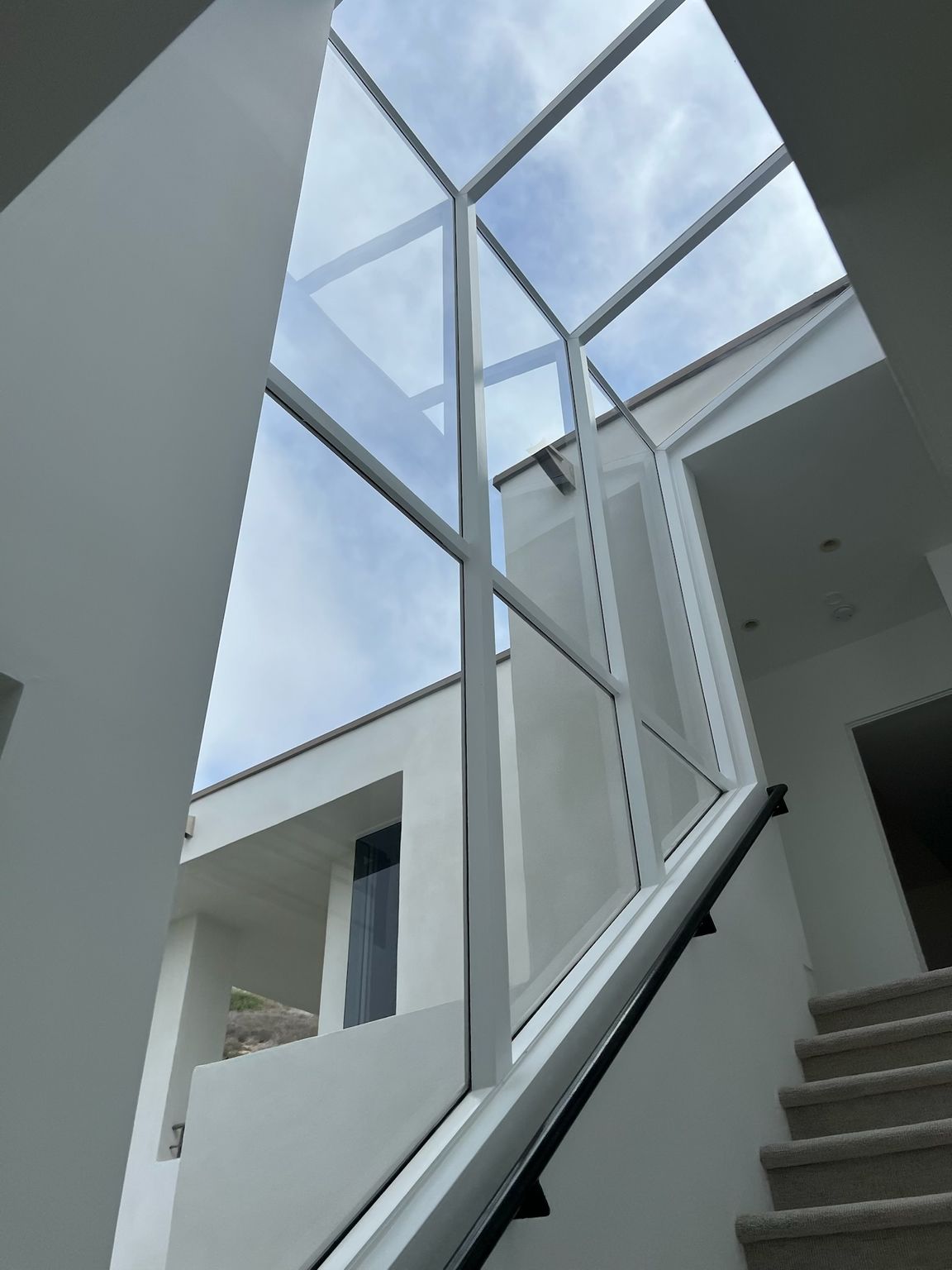 Modern stairwell with glass walls and skylight, showing stairs rising beside a bright open atrium.