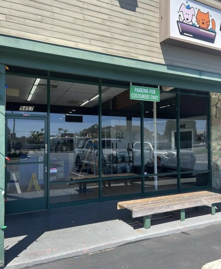 Storefront with large windows, green awning, and a bench outside on a sunny day.