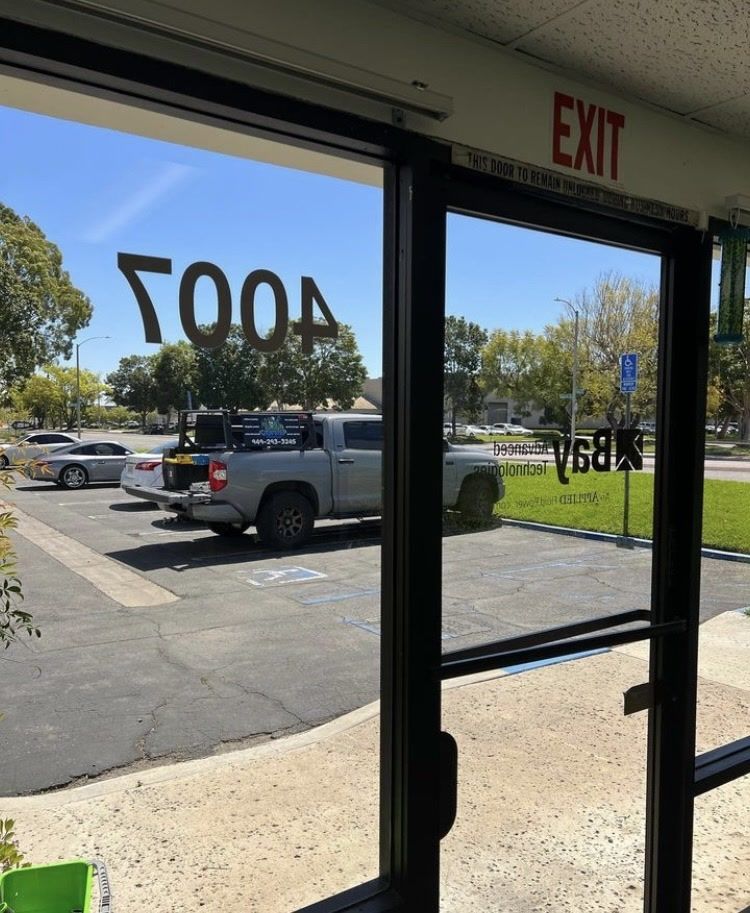 Storefront doorway with reversed 500 and 1880 window decals, looking out to a parking lot on a sunny day