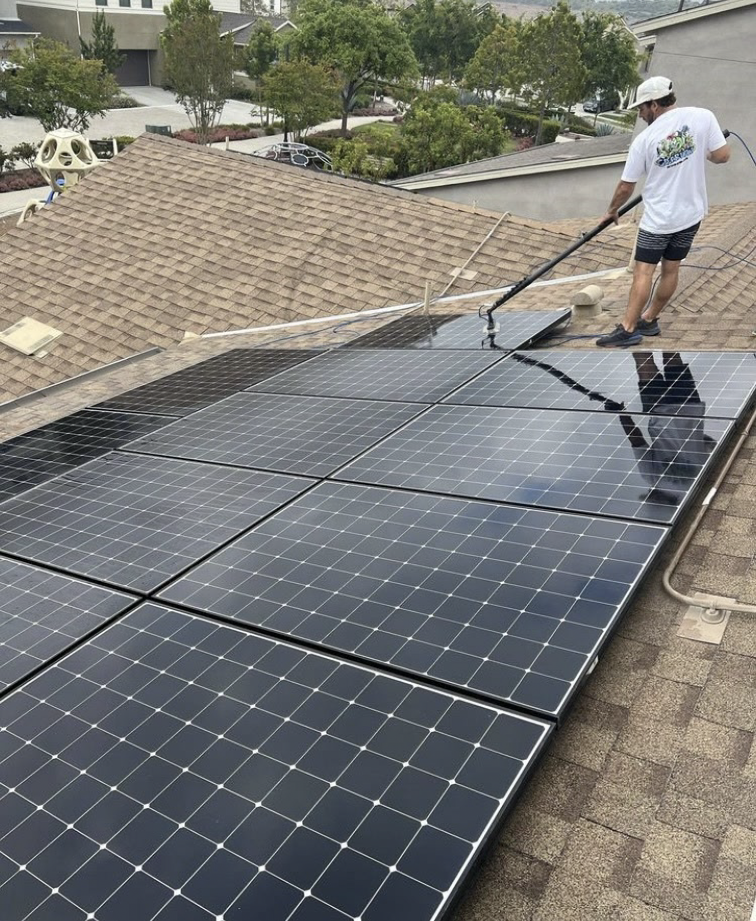 Worker installing solar panels on a rooftop, using a long tool over black panels.