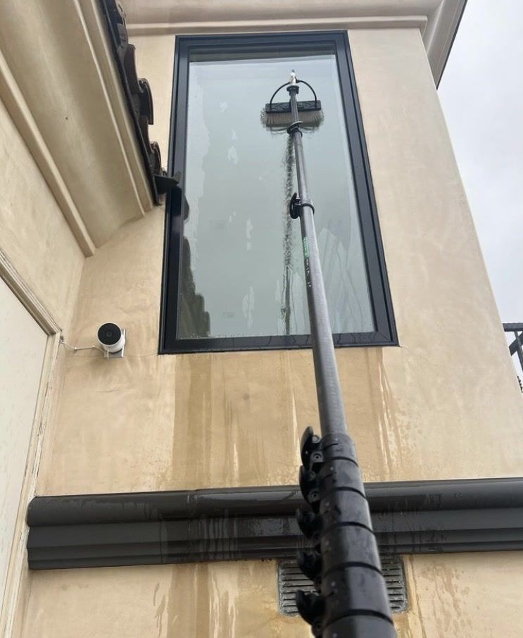 Tall pole with a device mounted in front of a beige building’s upper window and wall.