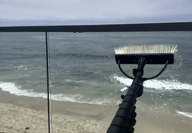 Beach view through a window, with a squeegee in the foreground and waves under a cloudy sky.