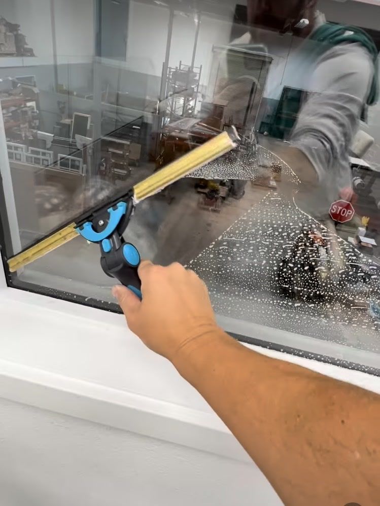 Hand using a blue suction-cup tool to press a yellow squeegee against a glass window.
