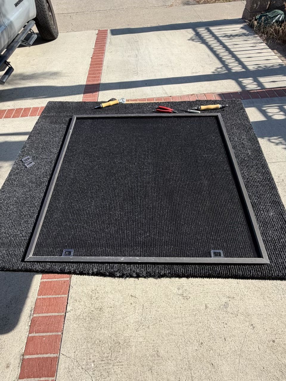 Black wheelchair ramp mat on a sidewalk near parked vehicle tires and brick-lined pavement