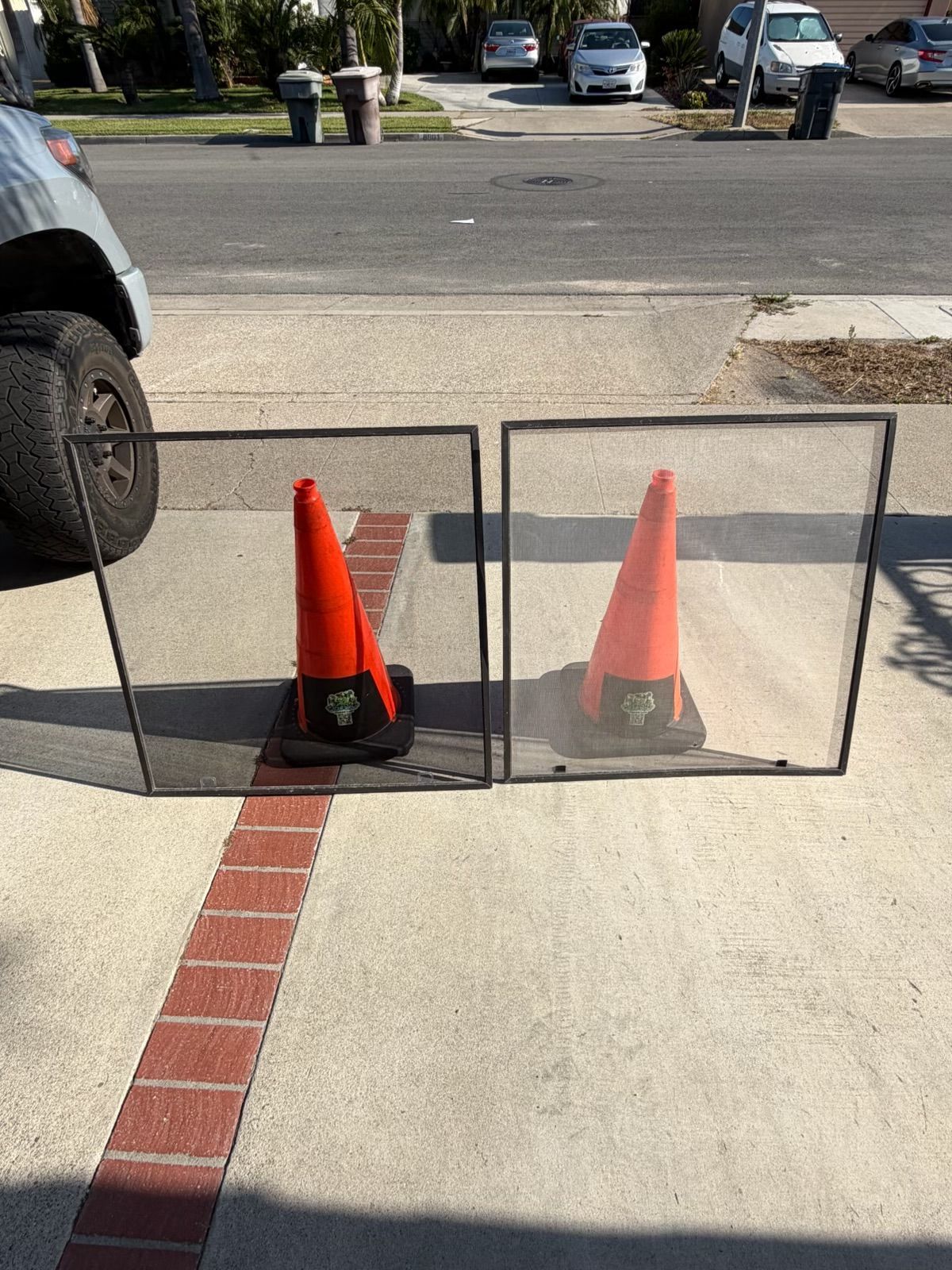 Two orange traffic cones blocking a sidewalk near a curb cut and red brick guide strip
