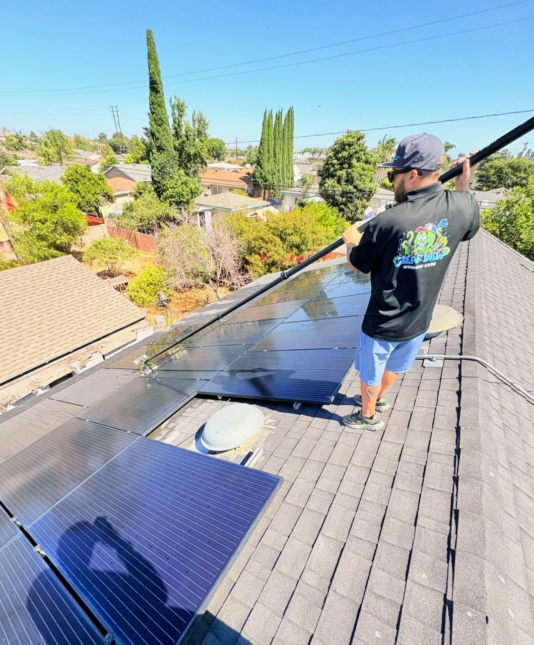 Worker on a tiled roof cleaning solar panels under a clear blue sky