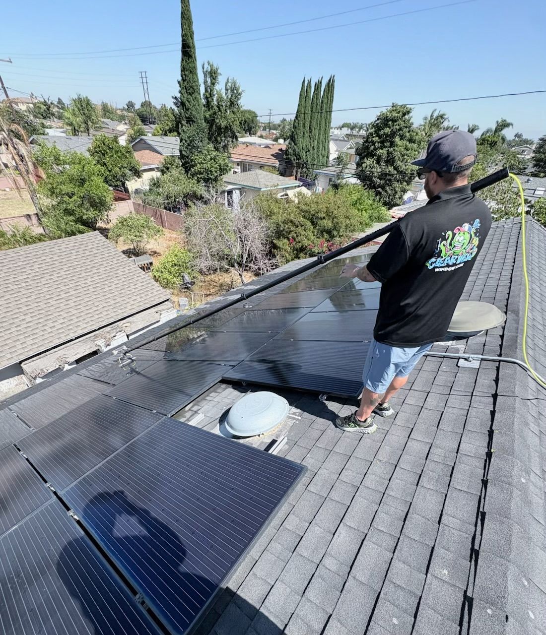 Worker spraying a rooftop with a pressure washer beside solar panels on a sunny day