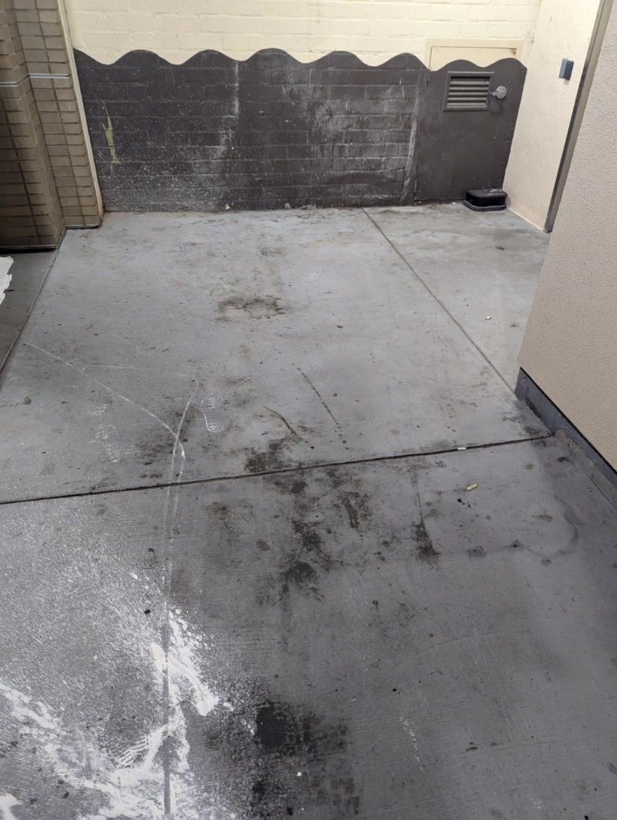 Concrete walkway with dark wet stains and debris near a wall and doorway.