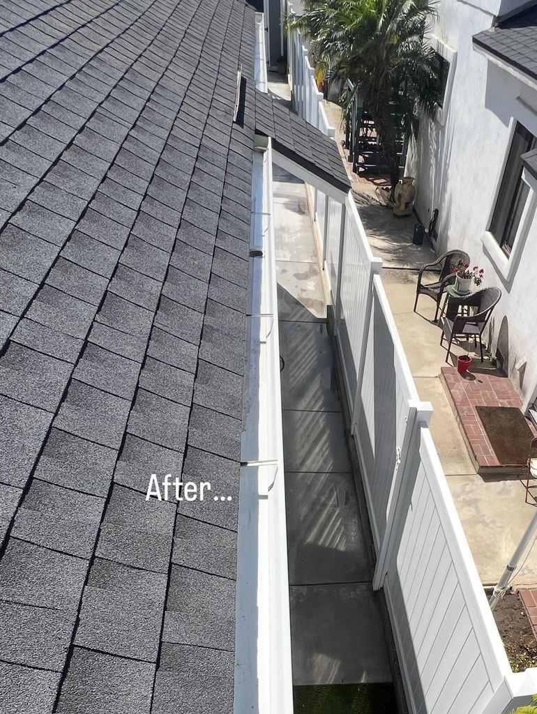 Narrow side yard between roof and white fence, with a concrete walkway and a tree at the end.