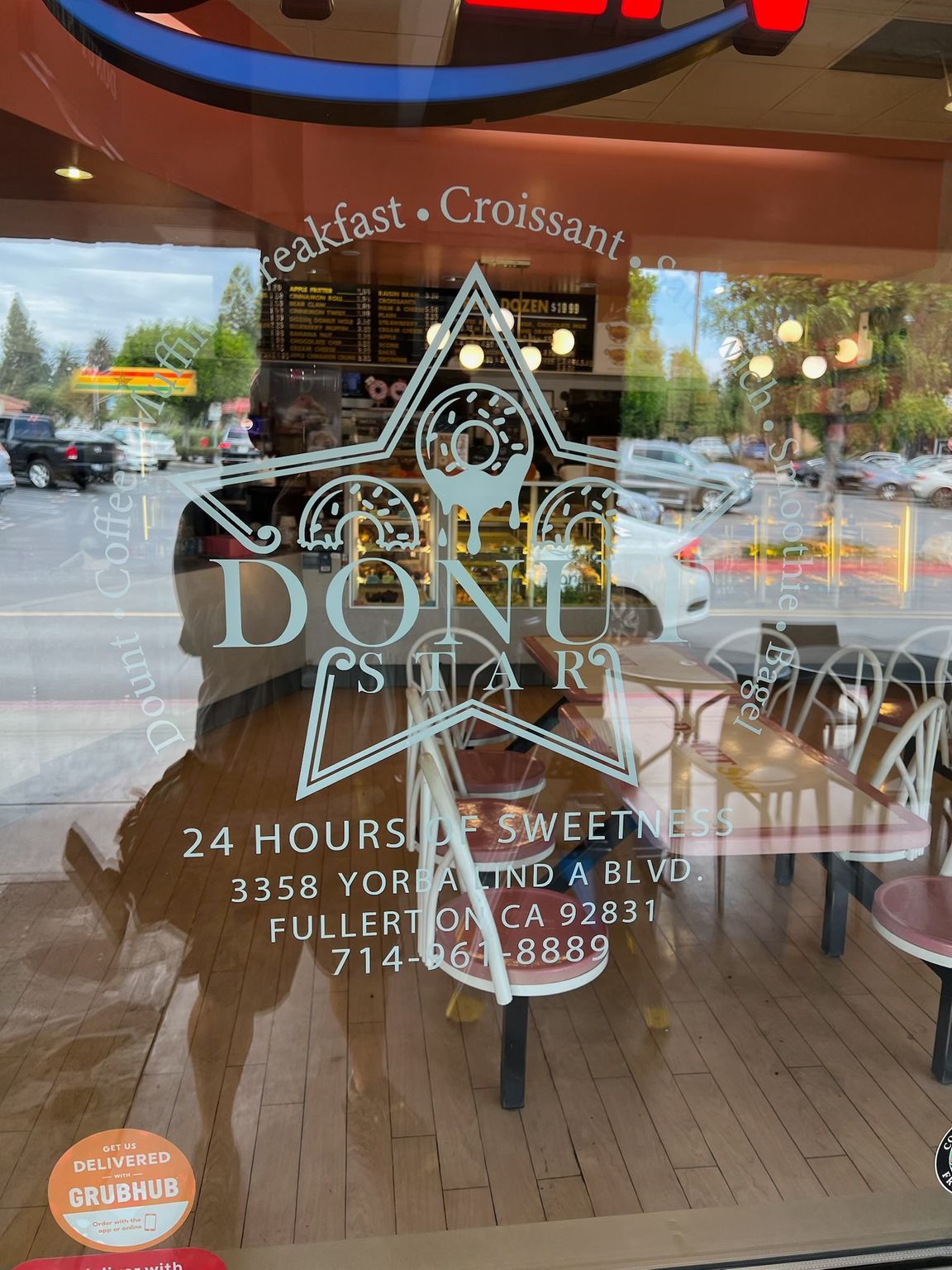Glass storefront door with white logo and hours, reflecting street and interior tables.
