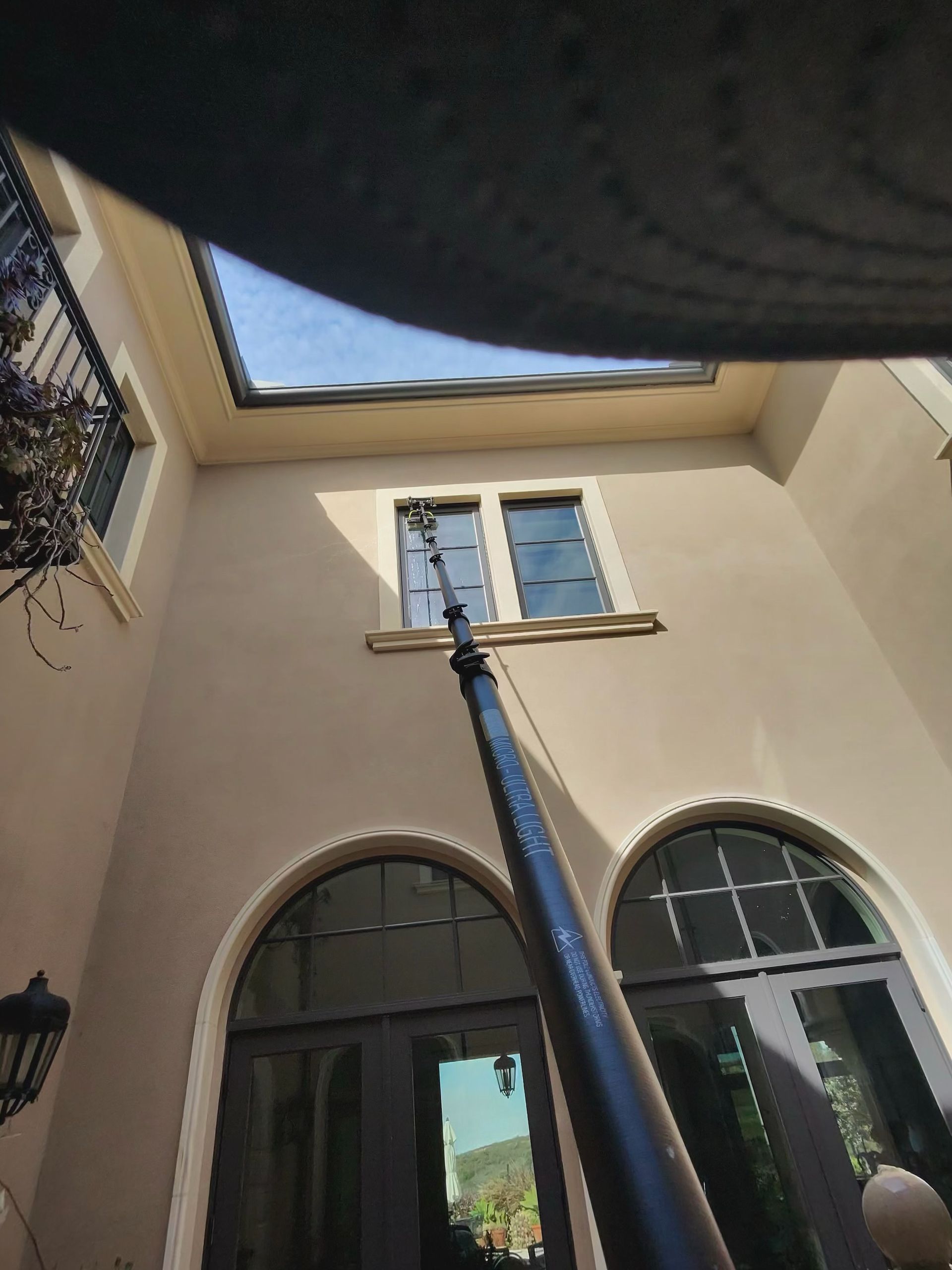 Courtyard view looking up at beige walls, arched windows, and a skylight with a blue pole centered below.