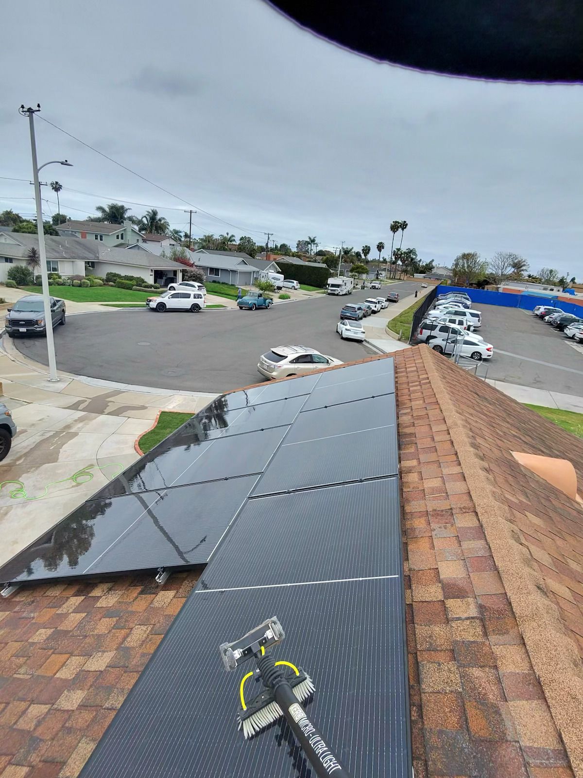 Solar panels on a shingle roof overlooking a residential street and parked cars