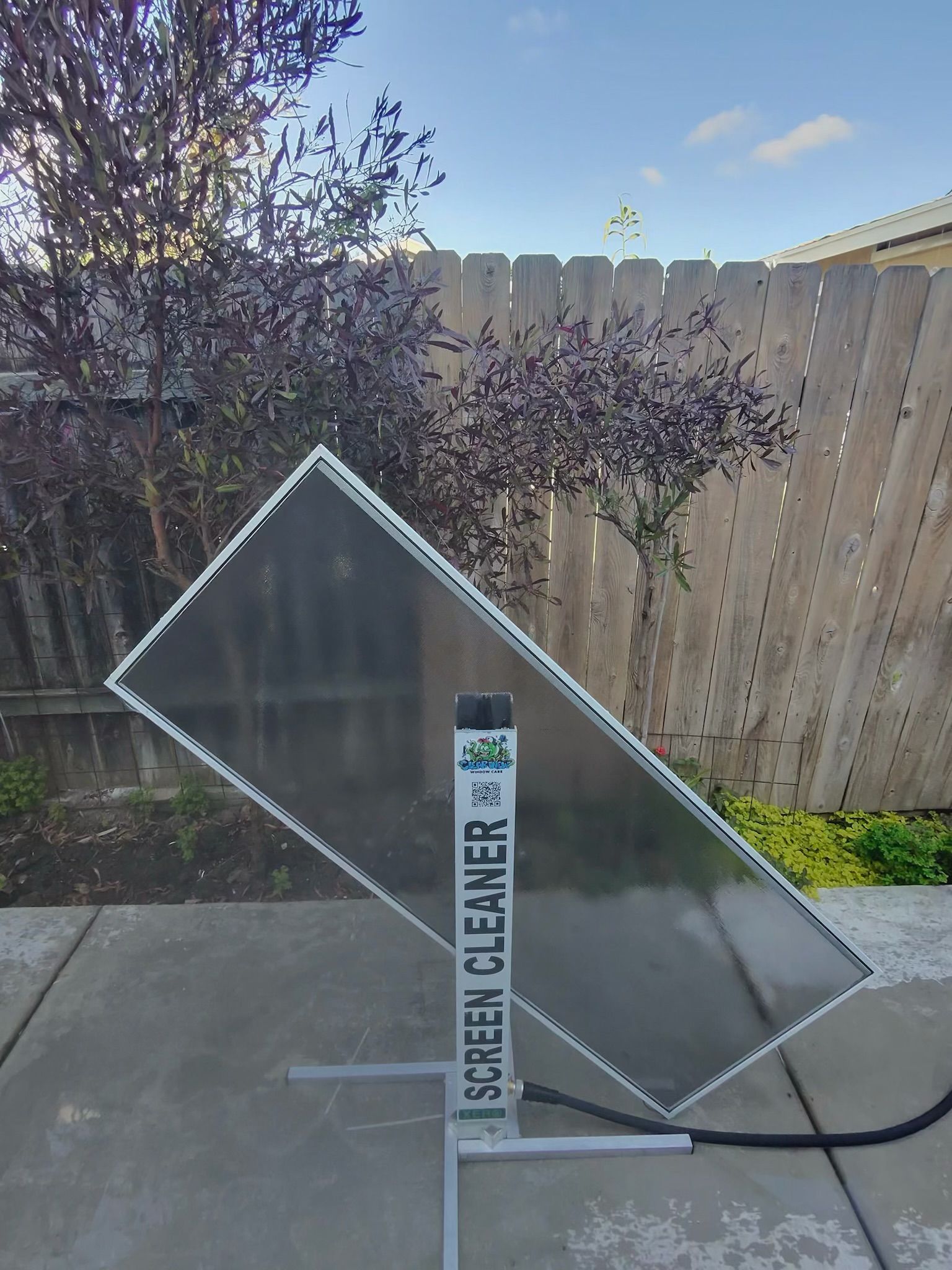 Tipped-clear sign with white frame leaning on a sidewalk in a backyard beside a wooden fence