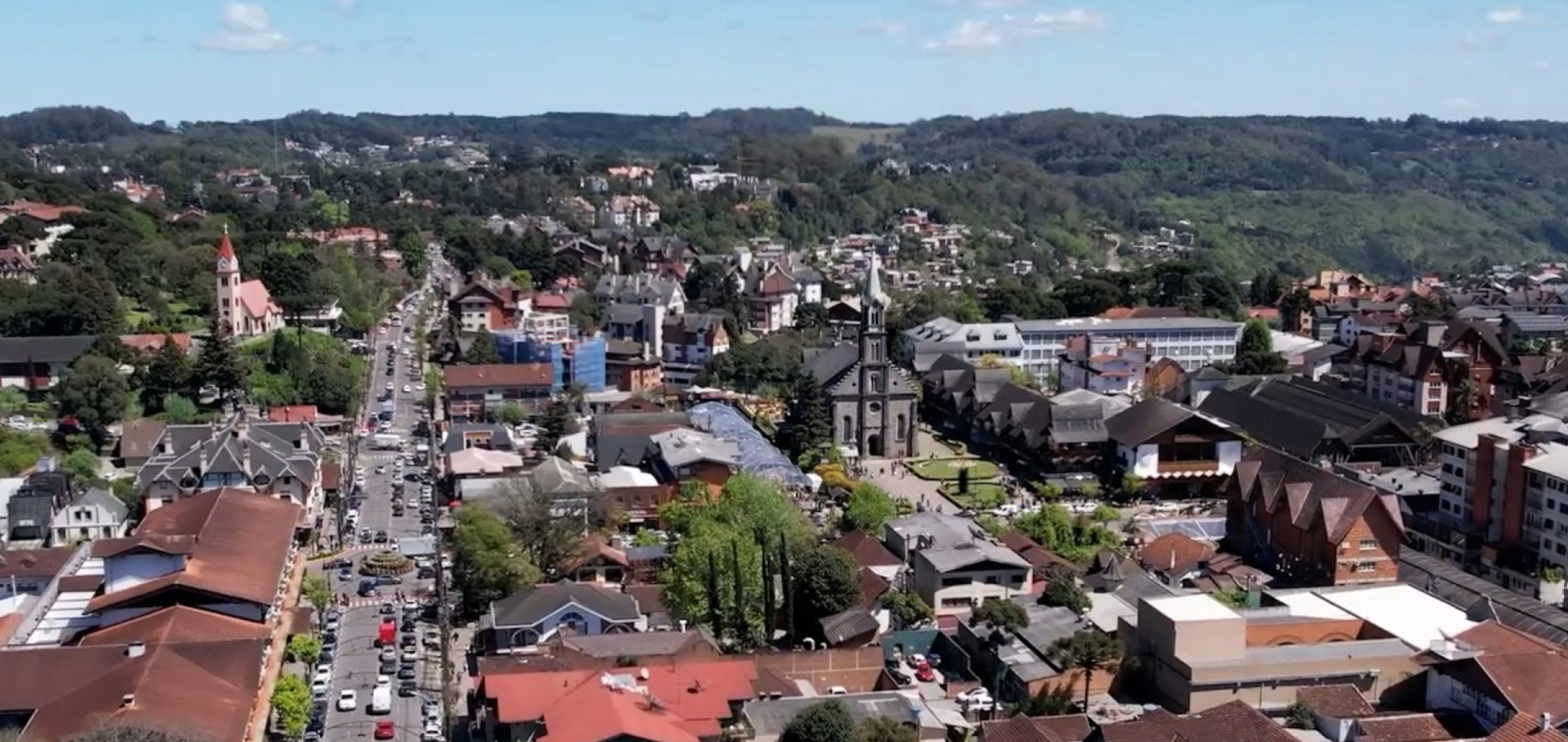 Aerial view of a town with red-roofed buildings, streets, and green hills in the distance