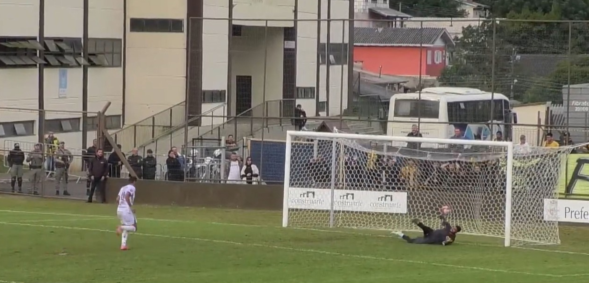 Soccer ball in the net as the goalkeeper dives in a match on a rainy field