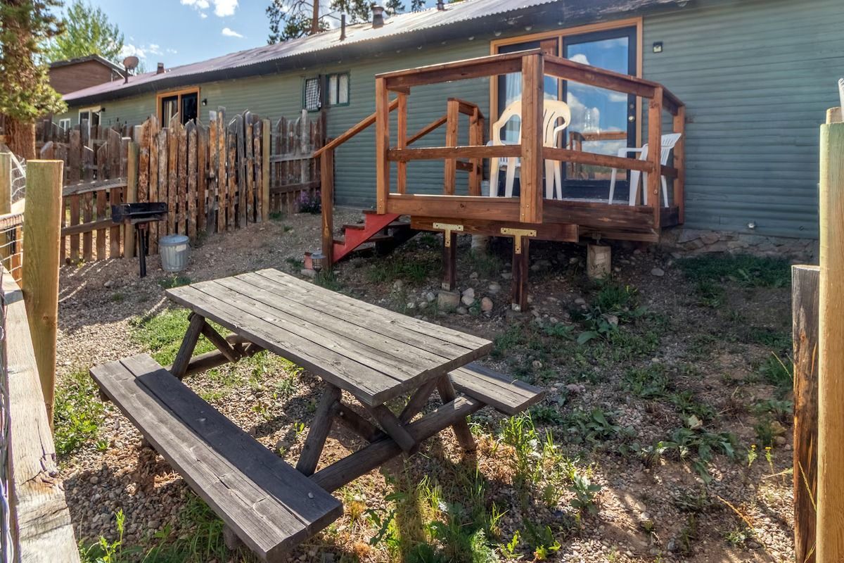Backyard with wooden picnic table, small deck, and house exterior in the background.