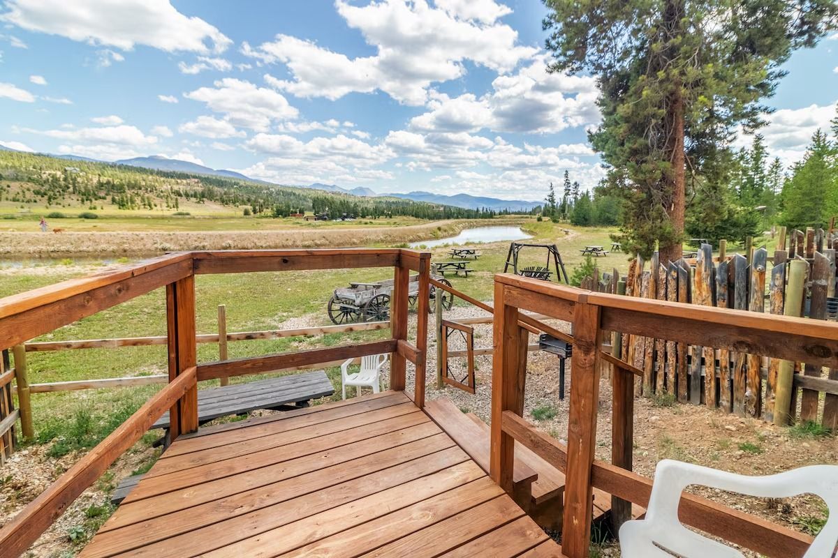 Wooden deck with railing overlooking a meadow and mountains under a partly cloudy sky