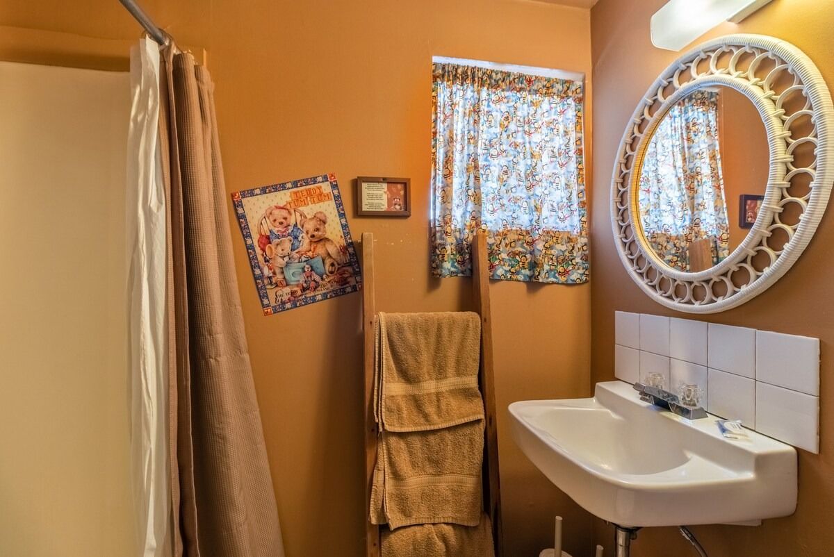 Small bathroom with beige walls, white sink, oval mirror, shower curtain, and folded towels hanging nearby