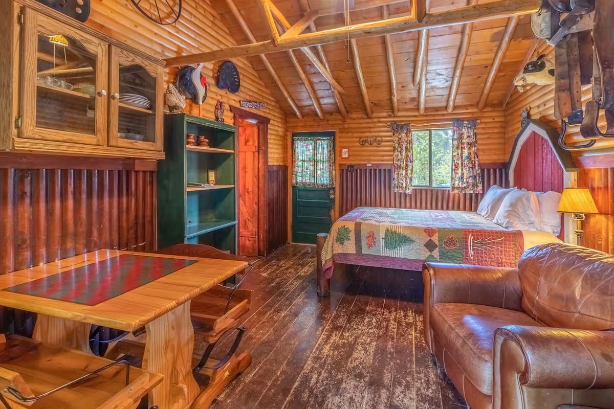 Cozy rustic cabin bedroom with wood-paneled walls, a bed, leather chair, and small dining nook