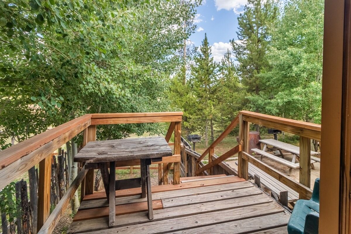 Wooden deck with railing and table overlooking green trees and a blue sky