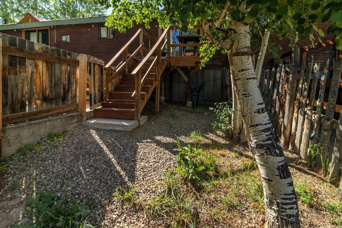 Backyard with wooden stairs, gravel ground, fence, and a birch tree in the foreground