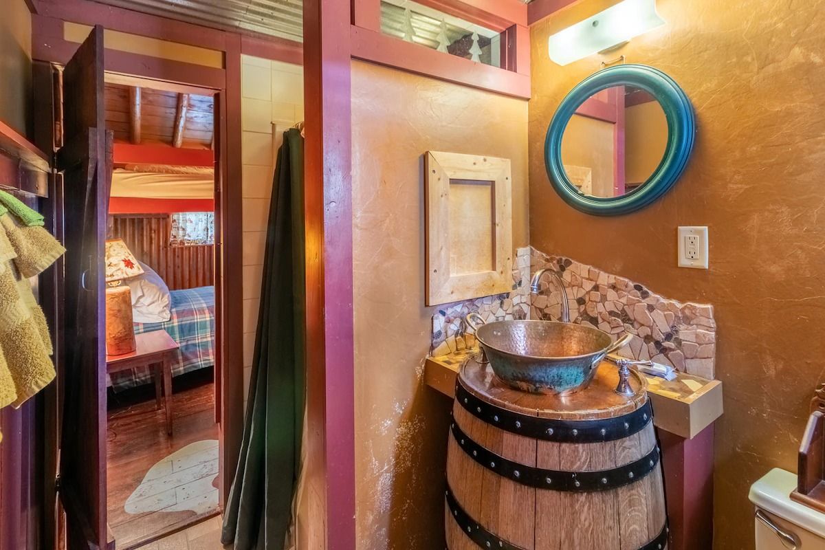 Rustic bathroom with wood barrel sink, round mirror, and adjacent bedroom doorway