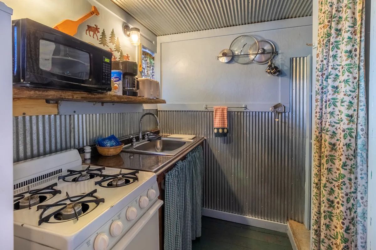 Small narrow kitchen with gas stove, sink, microwave, and corrugated metal wall panels
