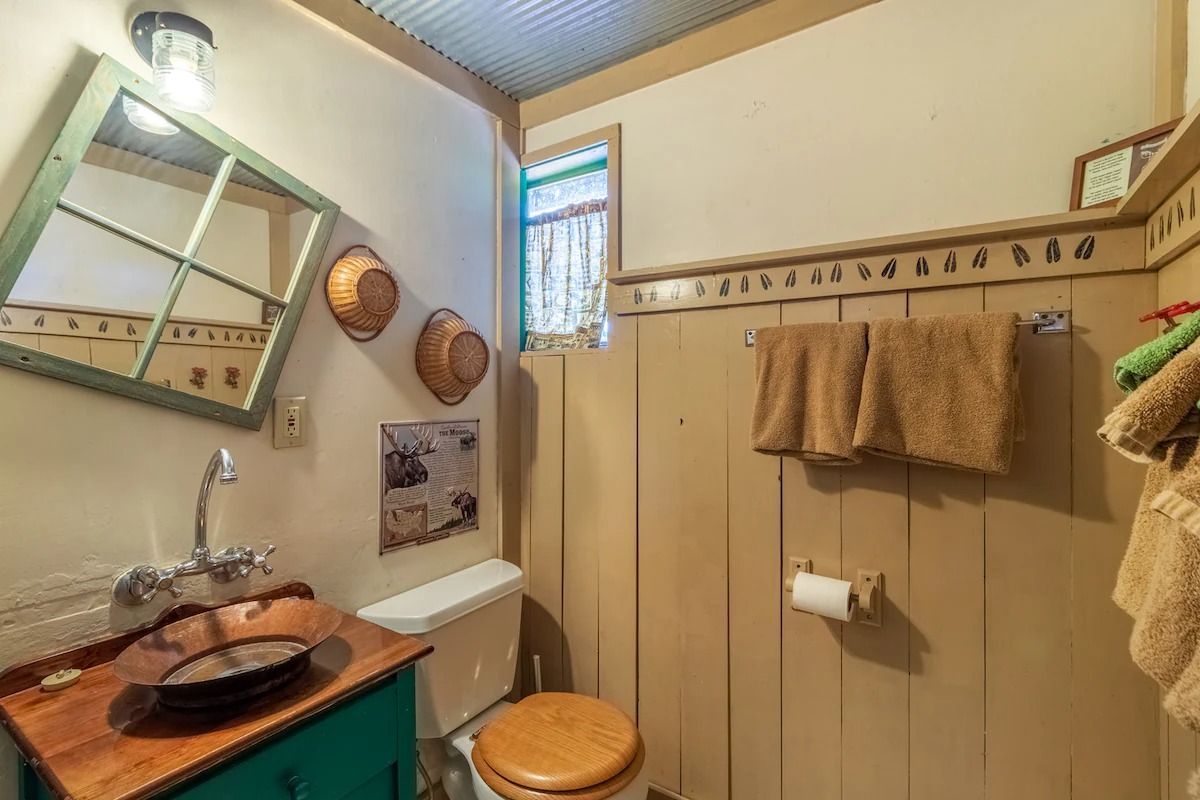 Small beige bathroom with sink, toilet, towel rack, mirror, and shower curtain.