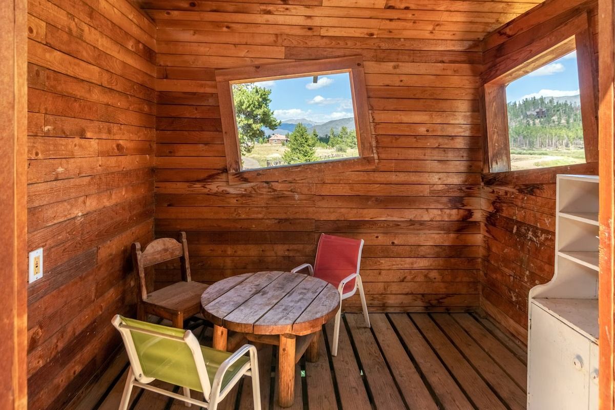 Wooden cabin interior with a small round table, chairs, and windows overlooking a mountain view