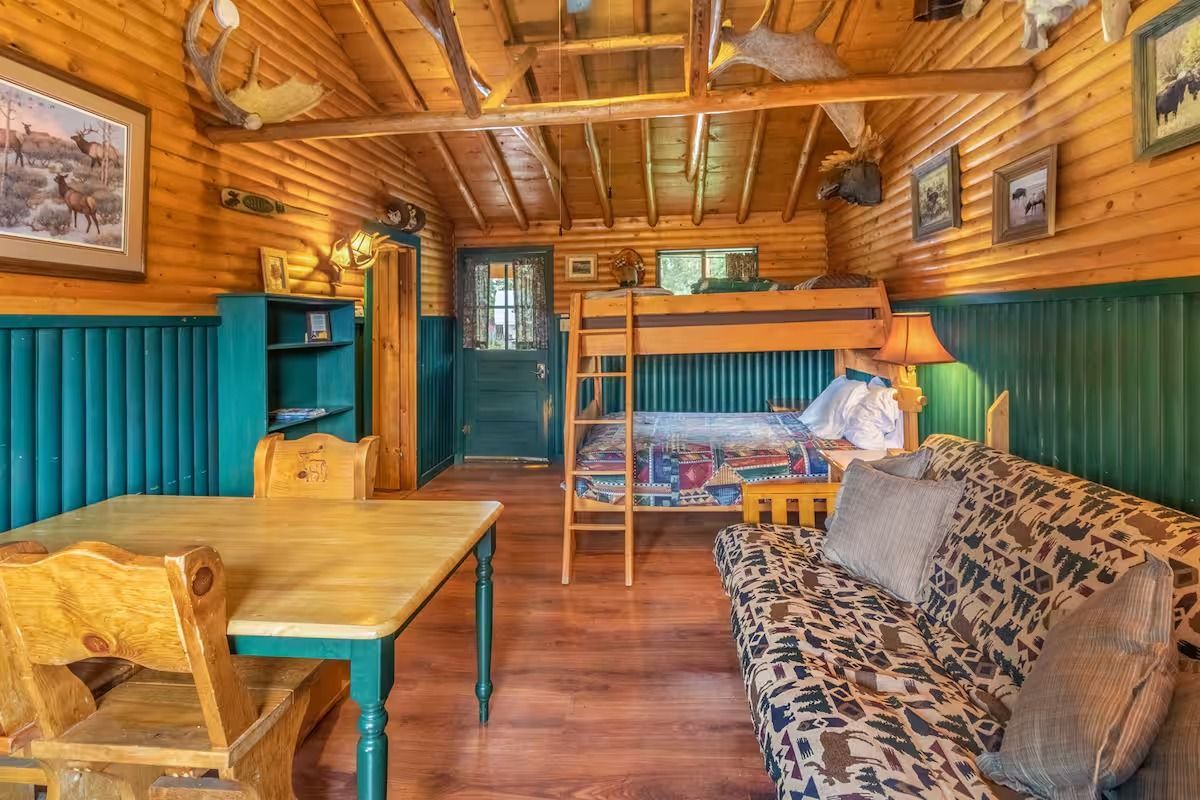 Rustic cabin interior with wooden walls, bunk bed, couch, table, and teal accents