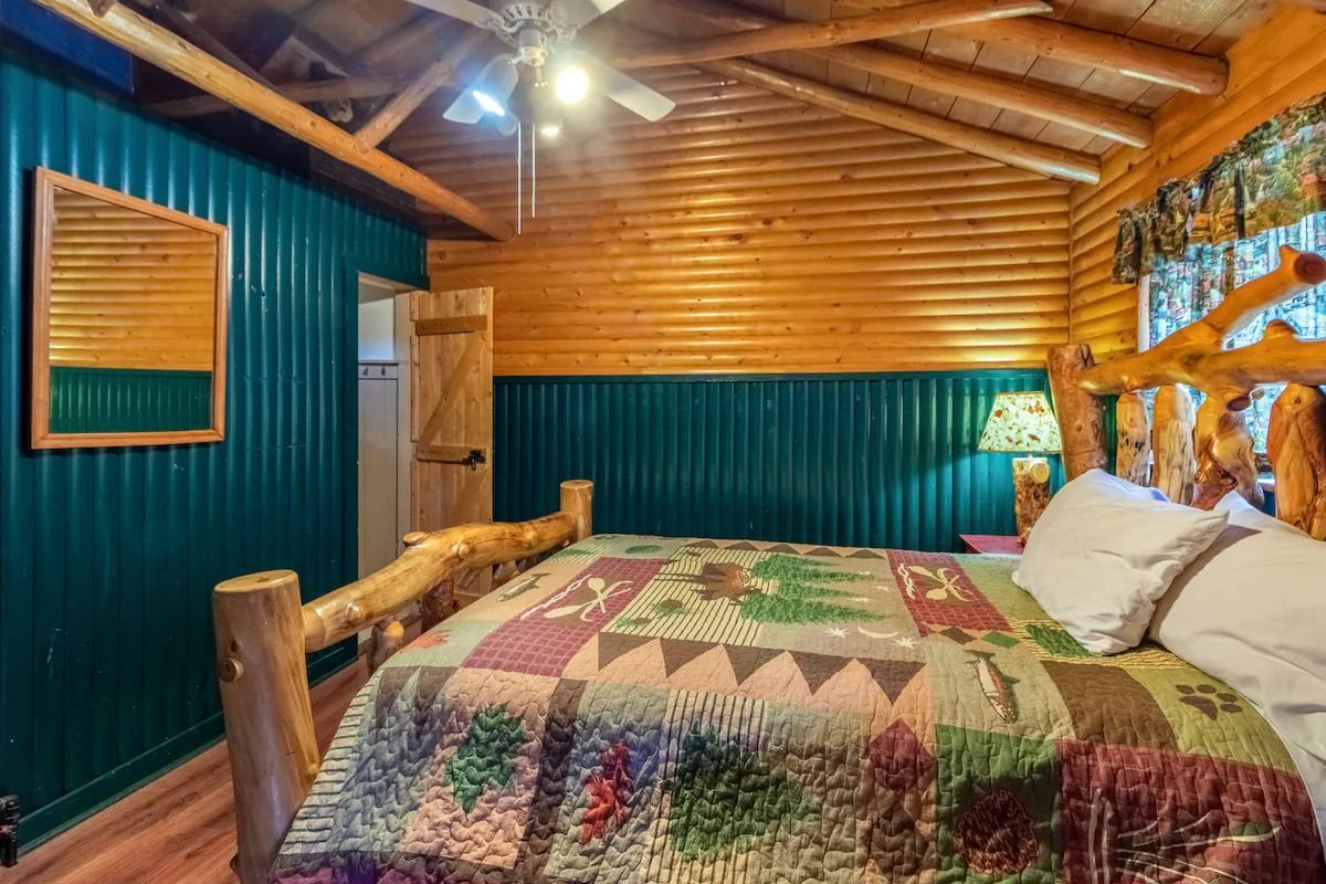 Rustic wood-paneled bedroom with log bed, quilted bedspread, and teal walls under a sloped ceiling