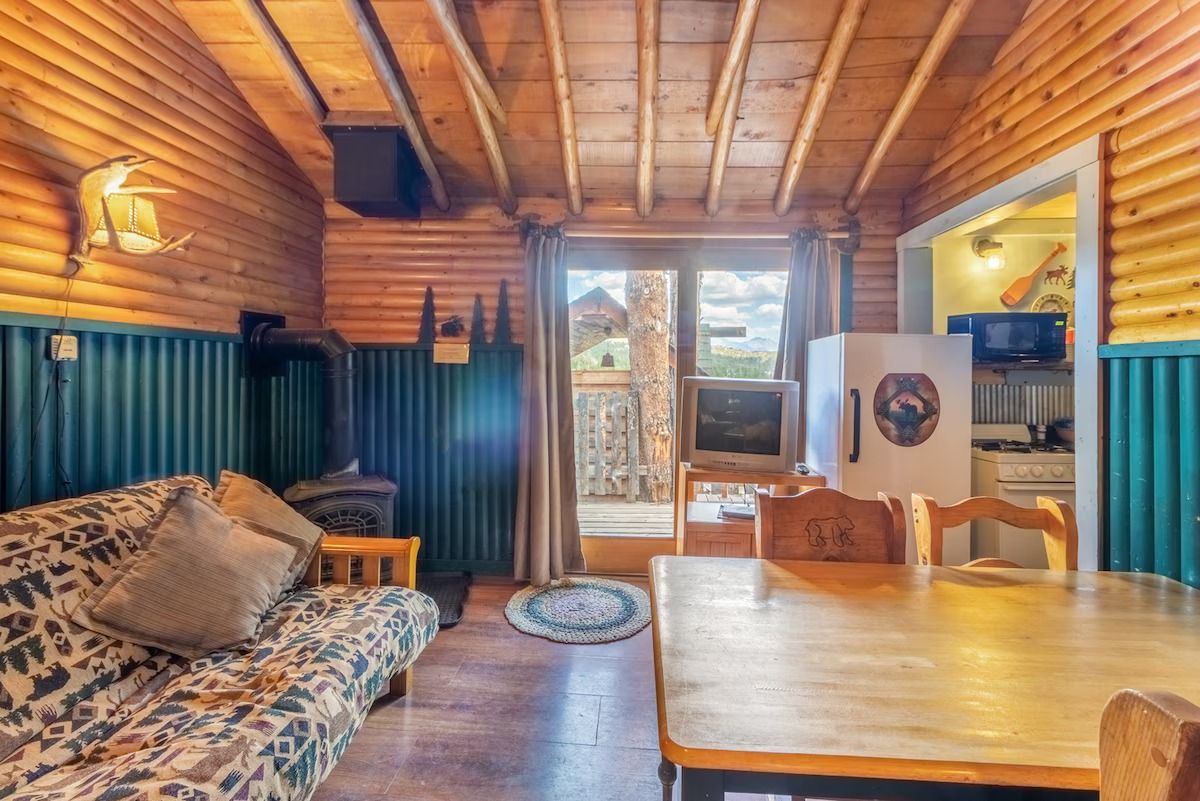 Cozy wood-paneled cabin living room with sofa, dining table, and glass doors to the outside
