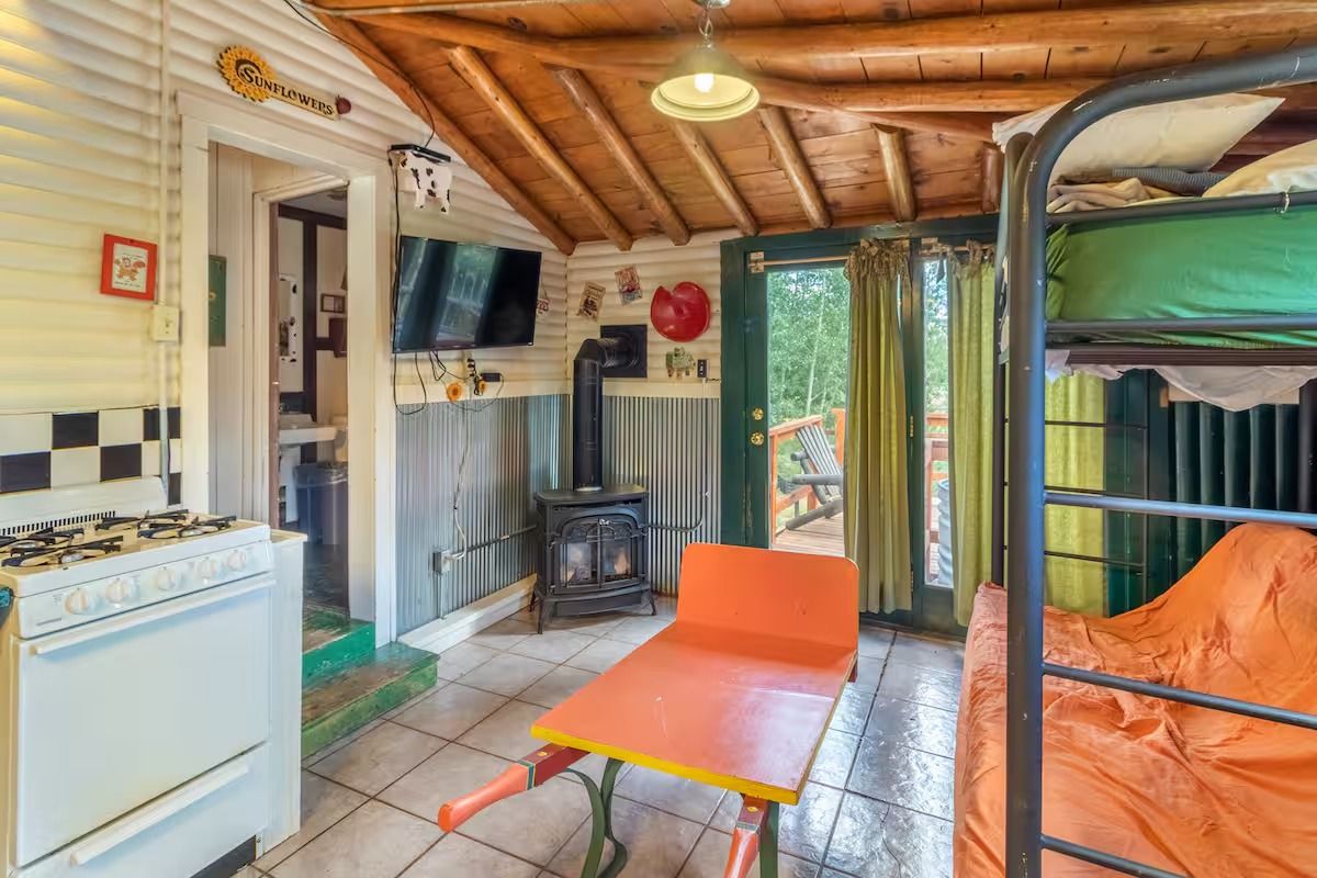 Cozy rustic kitchen with orange seating, tiled floor, wooden ceiling, and view of a porch with greenery