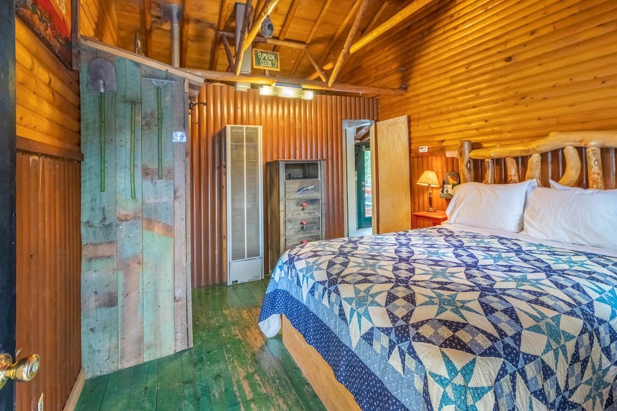 Rustic wood-paneled bedroom with a blue patterned quilt and a weathered painted door