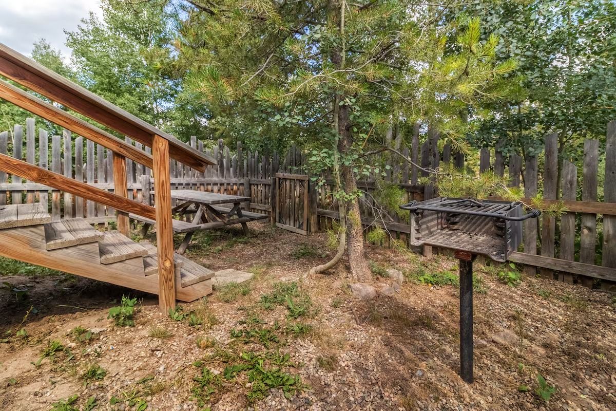 Wooden deck with stairs, picnic table, and grill in a wooded backyard setting