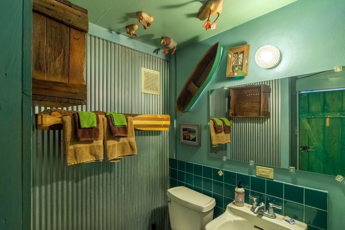 Turquoise bathroom with green shower curtain, towels, mirror, sink, toilet, and ceiling fish decor