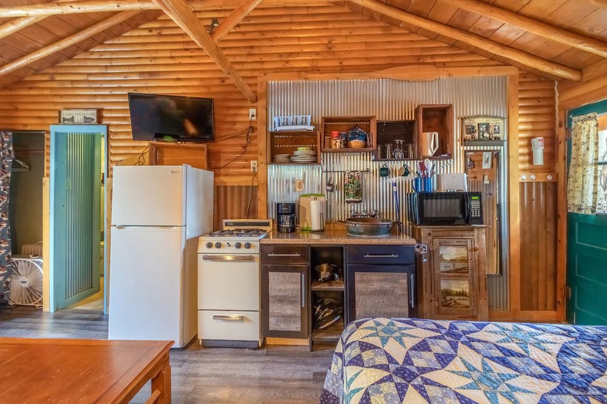 Rustic cabin interior with kitchenette, wood-paneled walls, white fridge, stove, and microwave