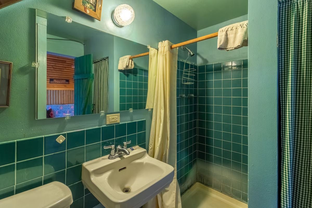 Turquoise-tiled bathroom with a sink, mirror, shower curtain, and towel rack