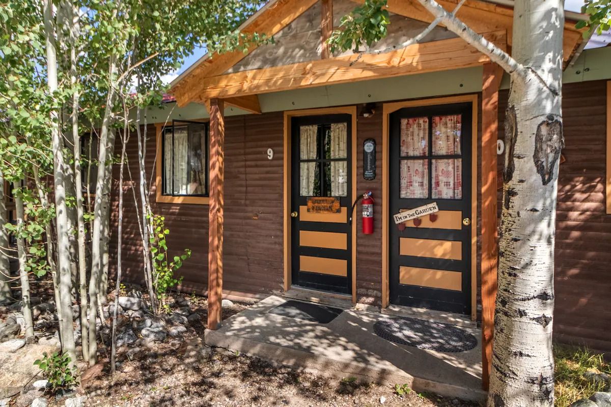 Rustic wooden cabin entrance with double doors, a window, and trees in front