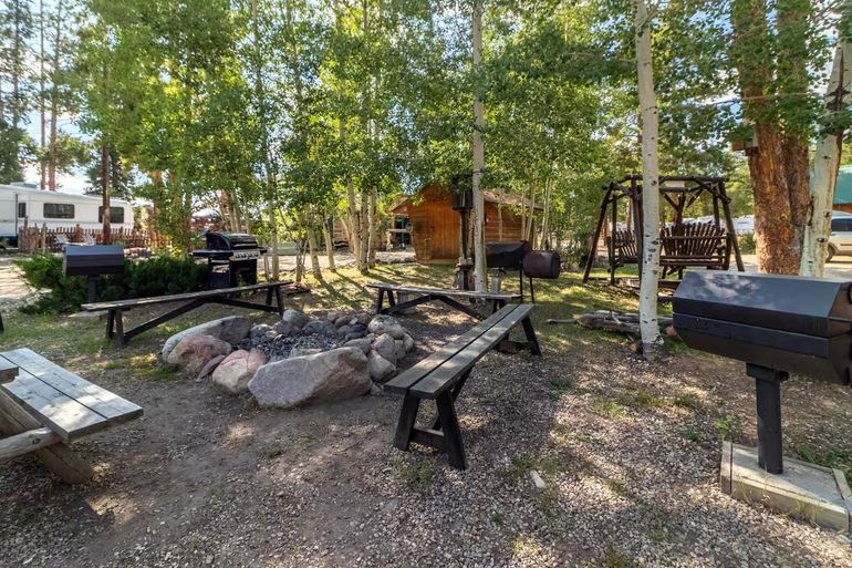Outdoor picnic area with picnic tables, grill, rocks, and trees in a wooded campsite area