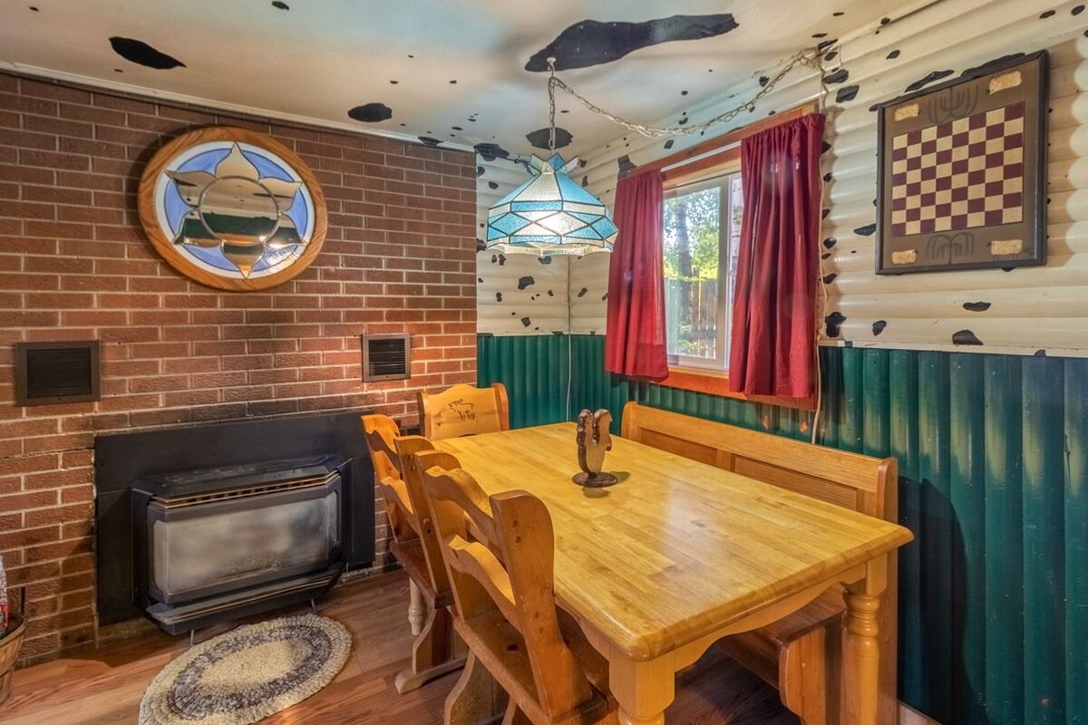 Cozy wood-paneled dining nook with brick fireplace, wooden table, red curtains, and nautical wall decor