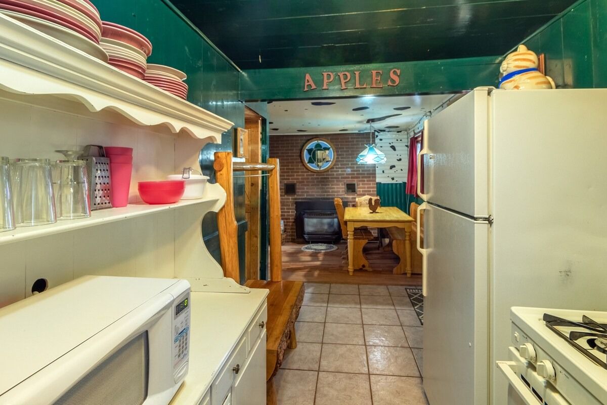 Narrow kitchen with white appliances, tiled floor, and teal walls leading to a dining area labeled “APPLES”