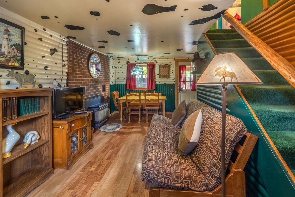 Cozy living room with wood paneling, patterned sofa, TV, dining nook, and staircase with green carpet