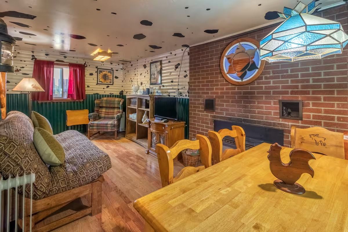 Cozy rustic dining room with wooden table, brick wall, patterned sofa, and stained-glass lamp