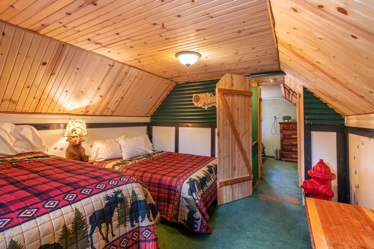 Cozy attic bedroom with two twin beds, wood-paneled ceiling, and a small sitting area