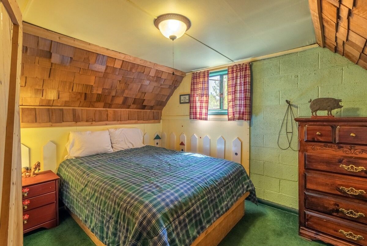 Cozy attic bedroom with a bed, wooden dresser, patterned curtains, and green walls